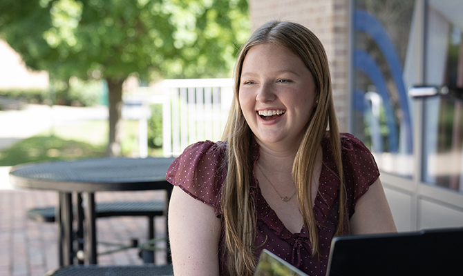 girl with burgandy shirt sitting at table with laptop