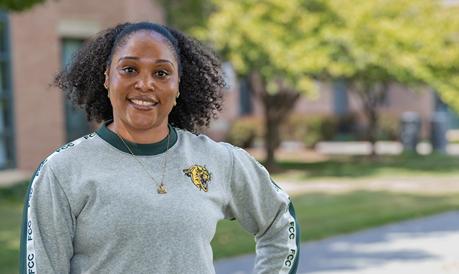 Woman in grey sweatshirt with gold cougar on chest and FCC printed down shoulders onto arms.